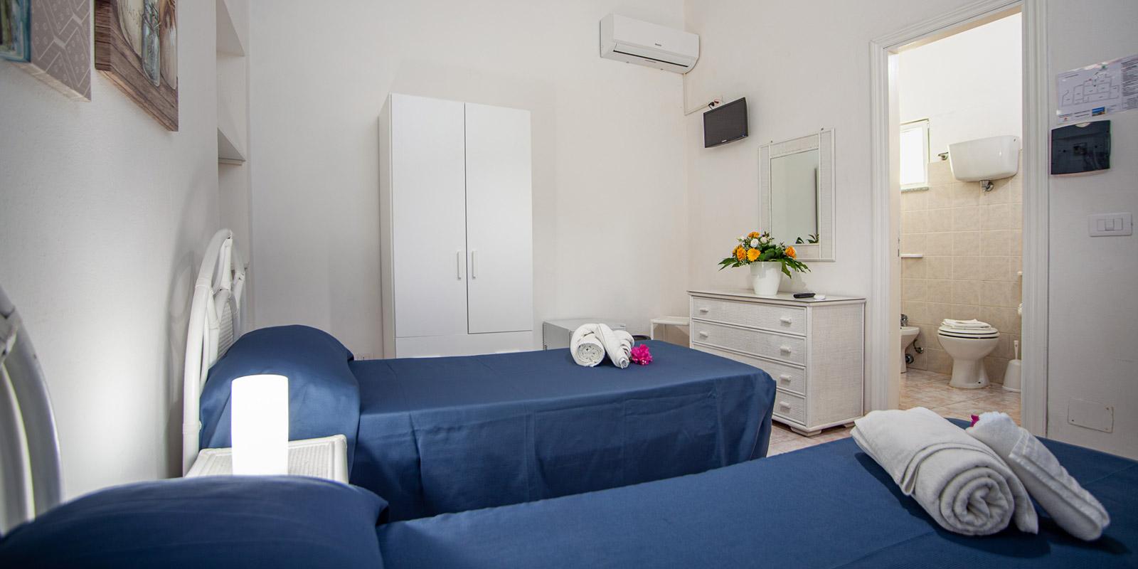Camera luminosa con letti singoli, bagno privato, armadio e decorazioni floreali.