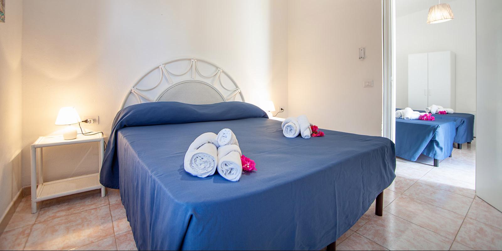 Camera da letto con letto matrimoniale, lenzuola blu e asciugamani bianchi arrotolati.