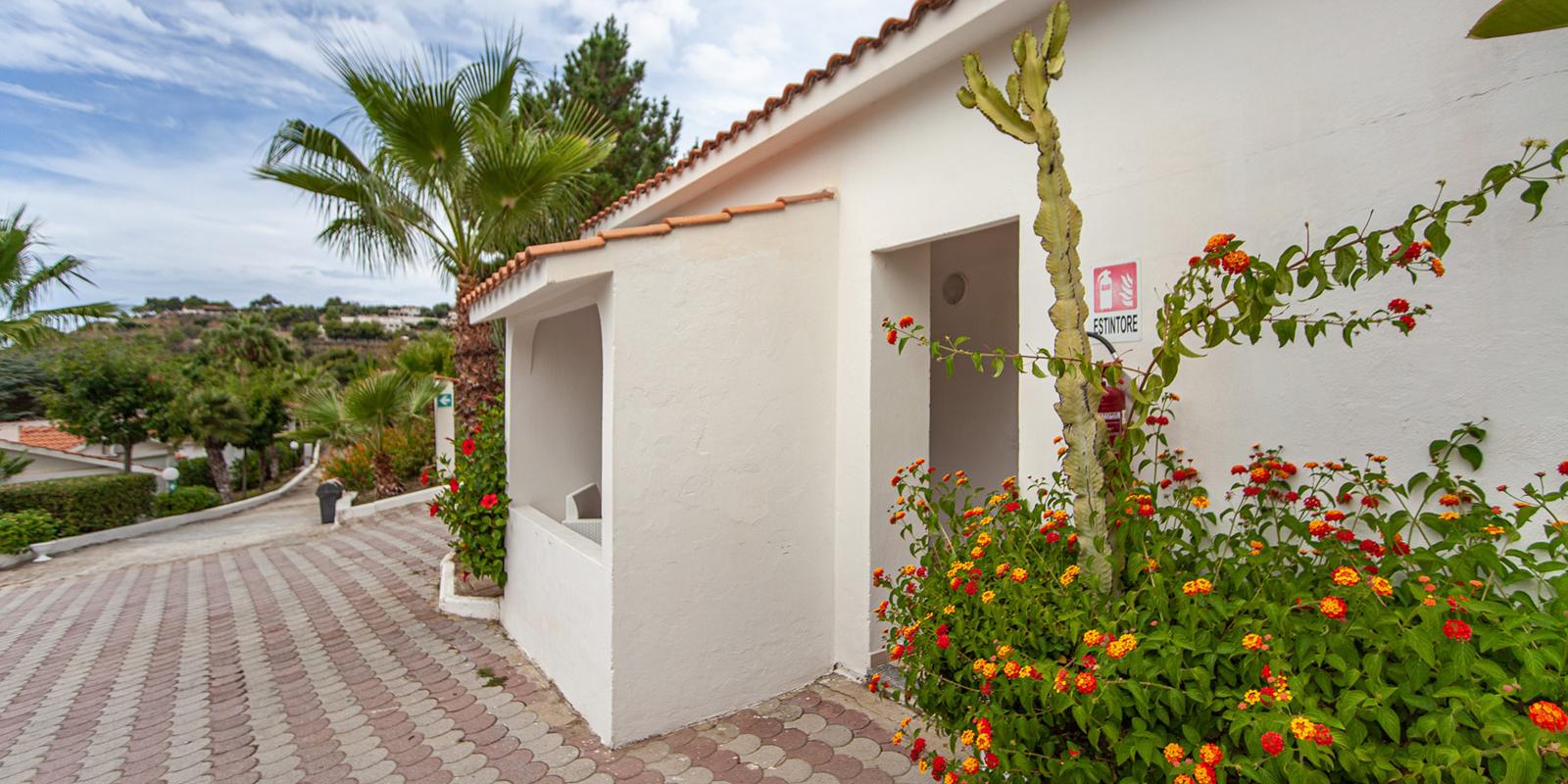 Casa bianca con piante tropicali e fiori colorati in un giardino soleggiato.