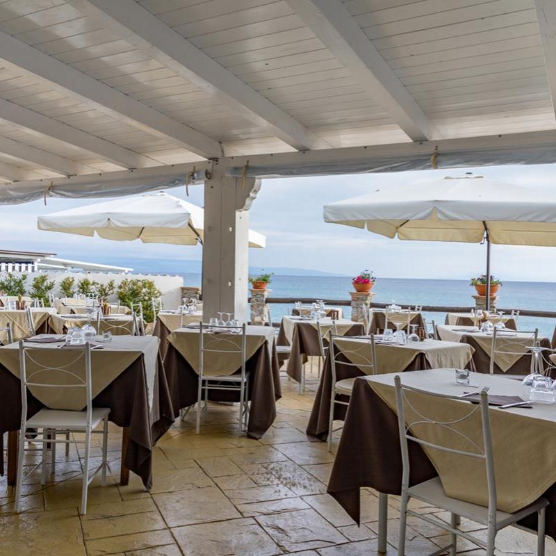 Ristorante sul mare con tavoli apparecchiati e ombrelloni, vista sull'oceano.